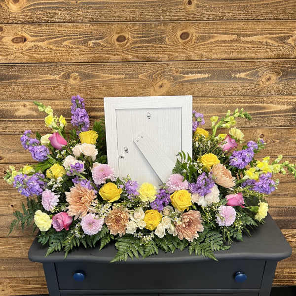Colorful floral arrangement around a white picture frame on a black cabinet