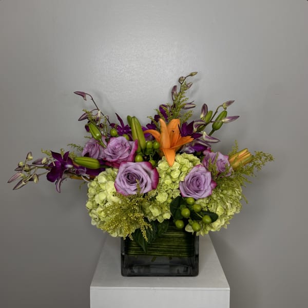 Lavender roses and orange lilies in a square glass vase