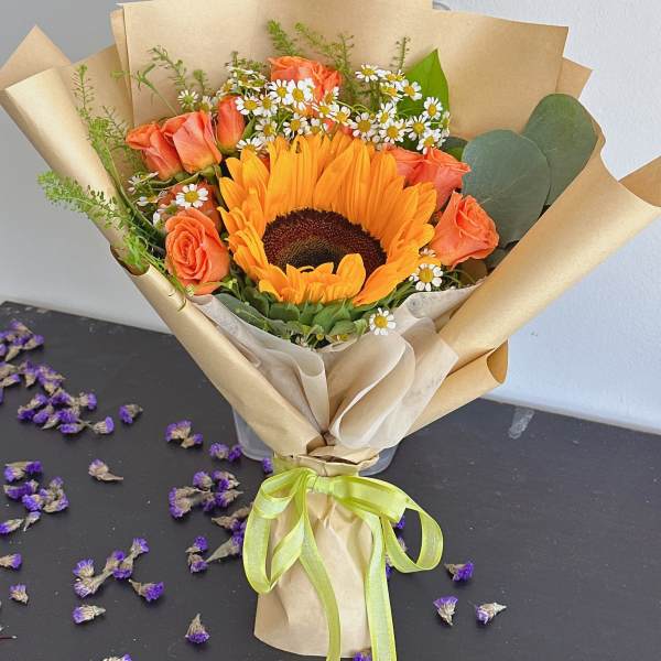 Bouquet with a sunflower, orange roses, and small white daisies in kraft paper