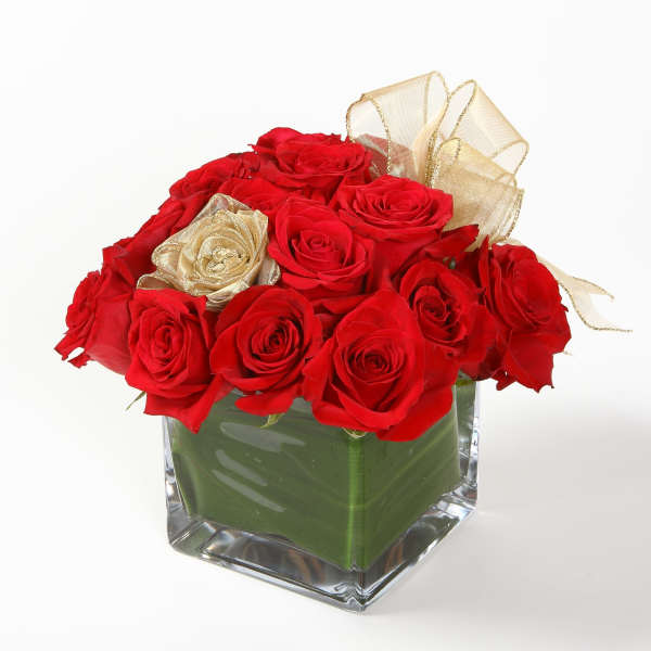 Red roses arranged in a clear square vase with gold ribbon accents