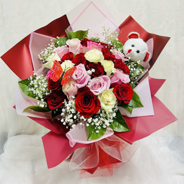 Bouquet of red, pink, and white roses with a small teddy bear