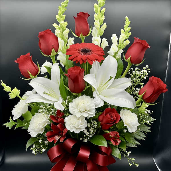Tall arrangement of red roses, white lilies, and carnations in a glass vase with a red bow
