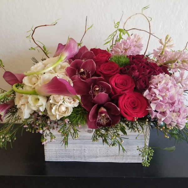 Arrangement of red roses, orchids, calla lilies, and pink hydrangeas in a white box