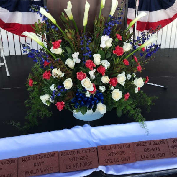 Large memorial floral arrangement with white calla lilies, roses, and blue flowers
