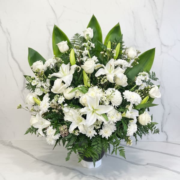 White lilies and roses in a black vase with green foliage