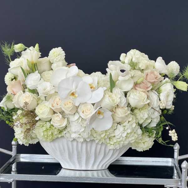 White floral arrangement in a white pedestal vase with pale blush roses and orchids