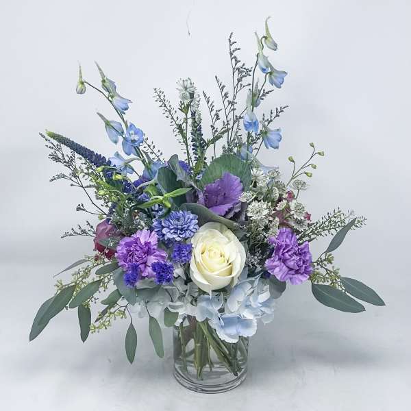 Mixed bouquet in a clear glass vase with blue, purple, and white flowers