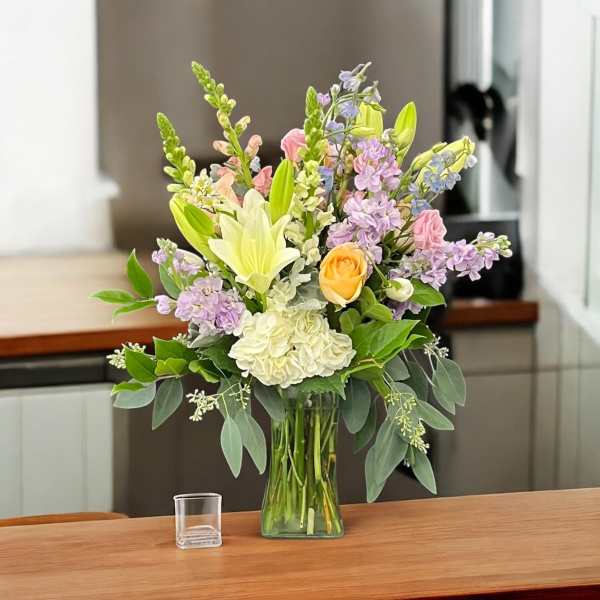 Pastel floral arrangement in a clear glass vase with lilies, roses, and hydrangea