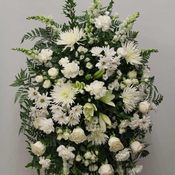 Tall white standing spray of roses, carnations, mums, and snapdragons on a green easel