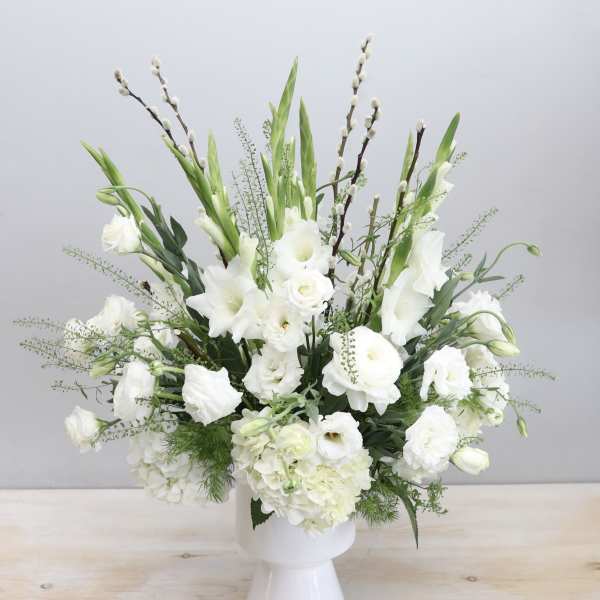 Tall white flower arrangement with lisianthus and ranunculus in a white pedestal vase