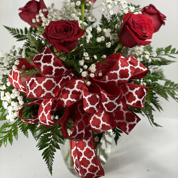 Red roses with baby's breath and a large red patterned ribbon in a glass vase