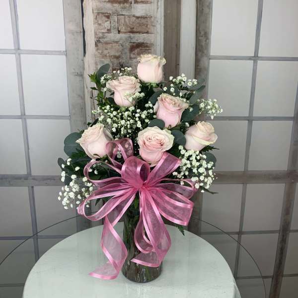 Pink roses arranged in a glass vase with a large pink ribbon