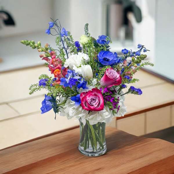 Colorful bouquet of roses, hydrangeas, and blue flowers in a glass vase