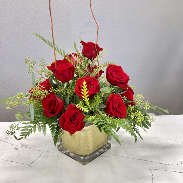 Red roses arranged in a clear square vase with greenery