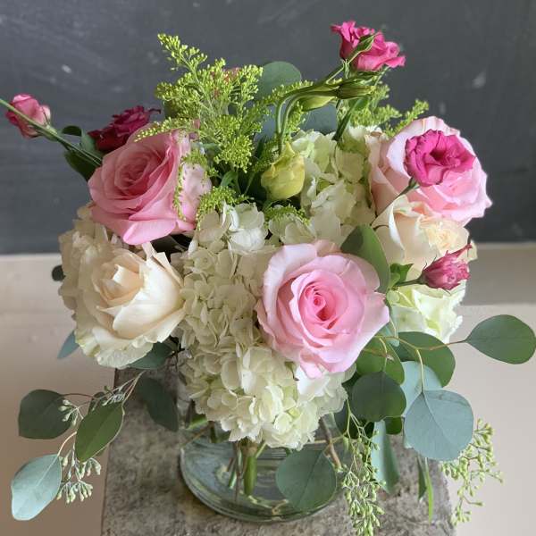 Pink and white roses arranged with hydrangeas in a glass vase
