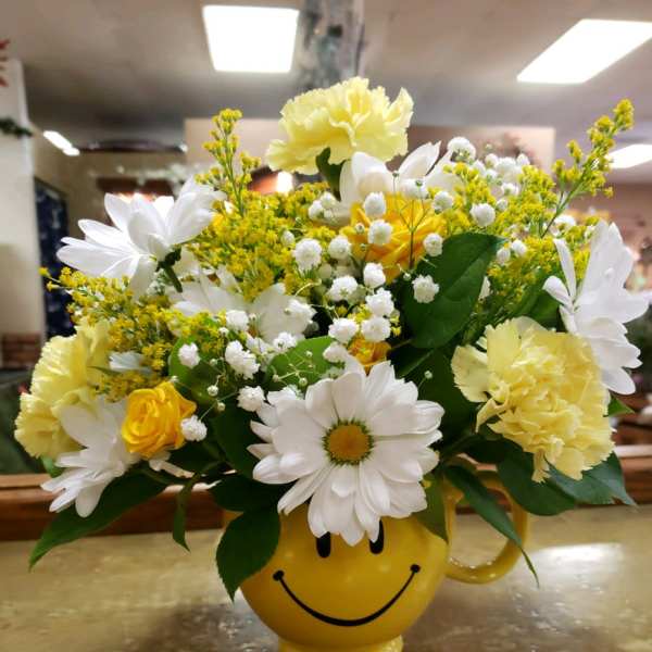 Yellow and white flower arrangement in a smiley-face mug