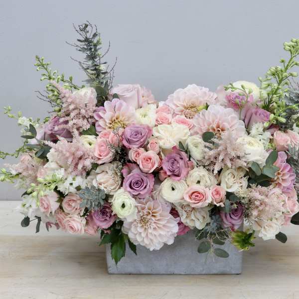 Low pastel arrangement of roses, dahlias, and ranunculus in a rectangular stone container