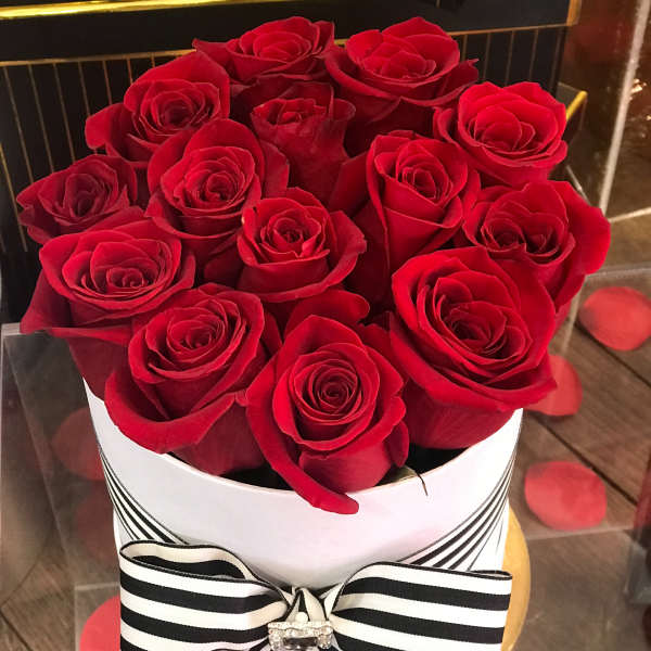 Red roses arranged in a white hat box with a black-and-white ribbon