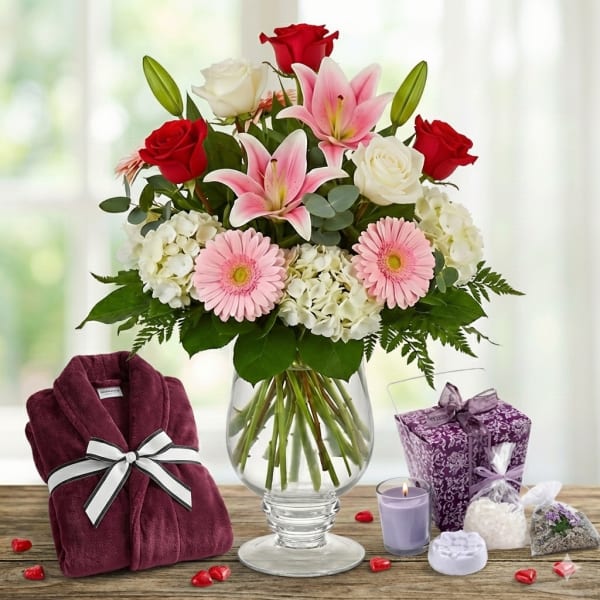 Mixed bouquet of roses, lilies and gerberas in a glass vase with robe and spa gift items.