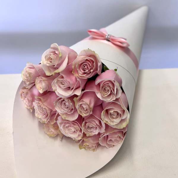 Bouquet of pale pink roses wrapped in white paper with a pink ribbon