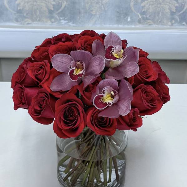 Red roses and pink orchids arranged in a clear glass vase