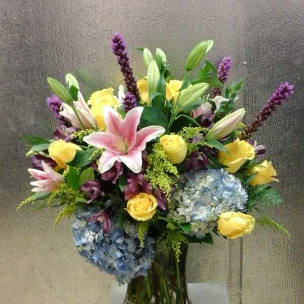 Bouquet of pink lilies, yellow roses, and blue hydrangeas in a glass vase
