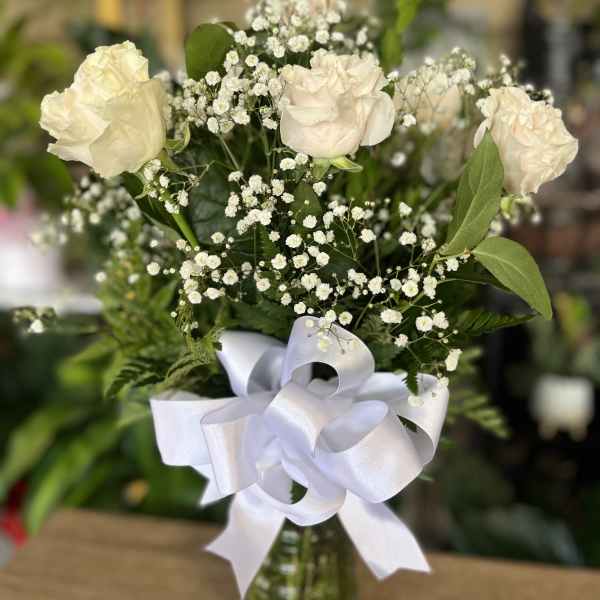 White roses with baby's breath in a glass vase tied with a white ribbon