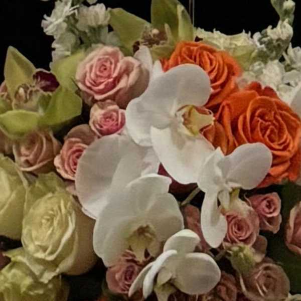 Compact arrangement of white orchids and orange and blush roses in a black vase