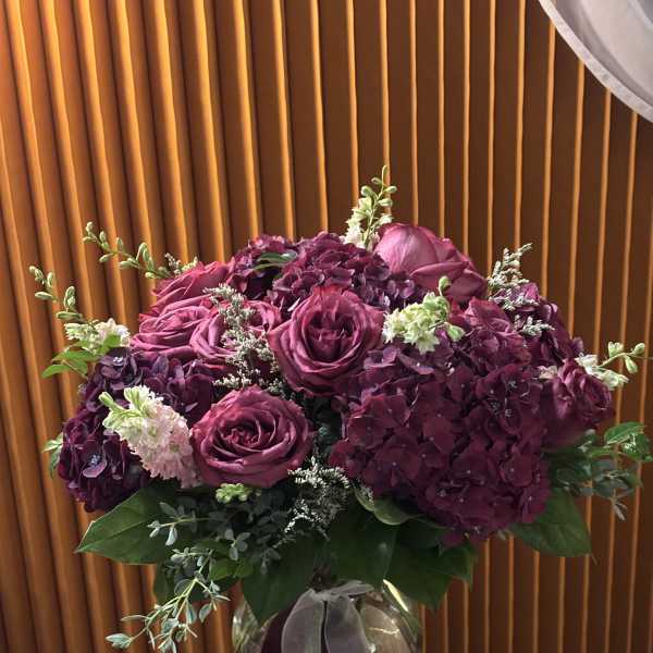 Purple roses and hydrangeas in a glass vase with ribbon
