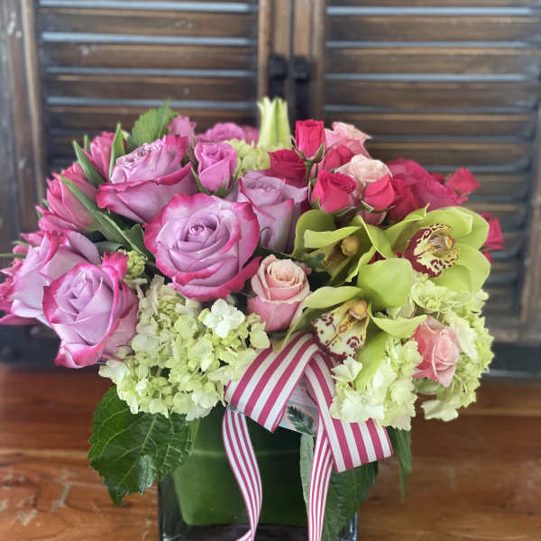 Pink and lavender roses with green orchids in a square vase