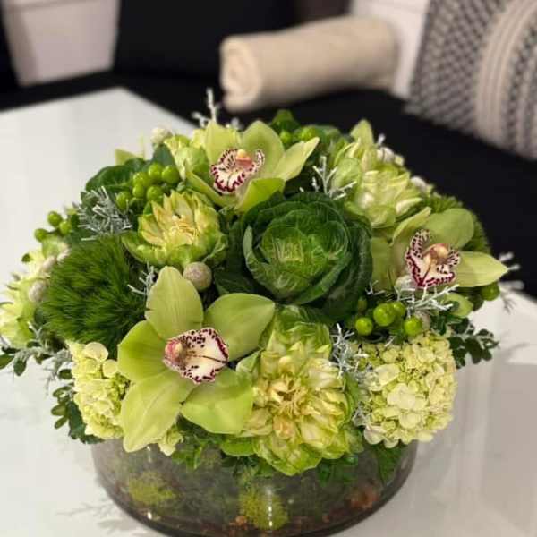 Green floral arrangement in a low glass bowl with orchids and hydrangeas
