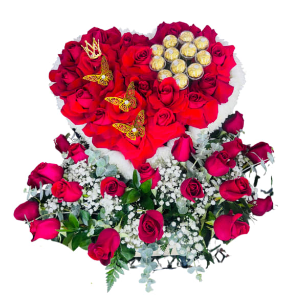Heart-shaped arrangement of red roses with chocolates above a bed of red roses and white filler flowers