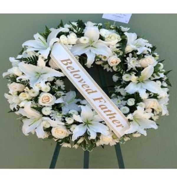 White funeral wreath with lilies and roses on a stand