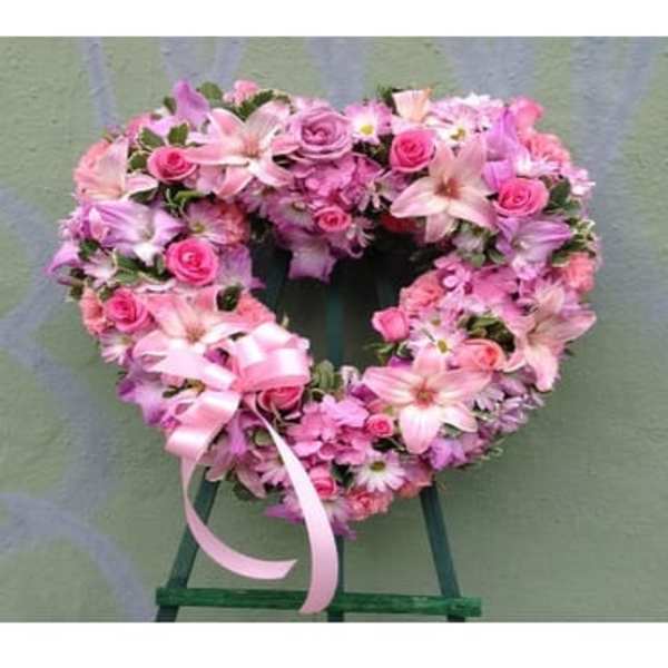 Heart-shaped pink floral wreath on a stand with ribbon