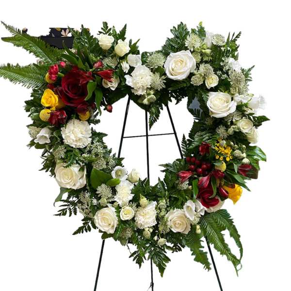 Heart-shaped floral wreath on a stand with white, red, and yellow roses