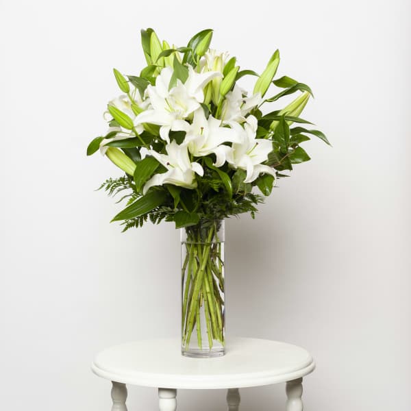 White lilies arranged in a tall clear glass vase