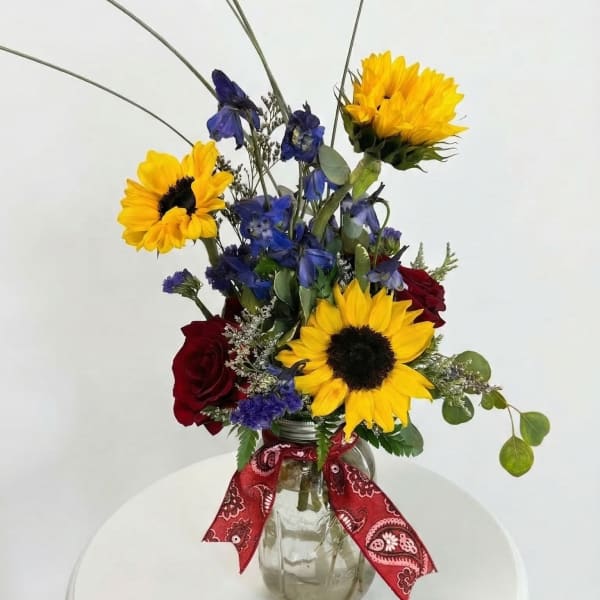 Bouquet of sunflowers, blue flowers, and red roses in a glass jar vase