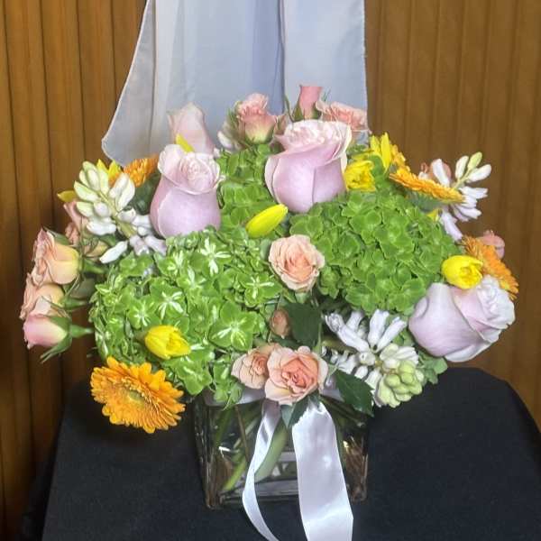 Pink roses and yellow-orange flowers in a glass vase with a white ribbon