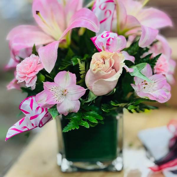 Pink lilies and roses arranged in a square glass vase