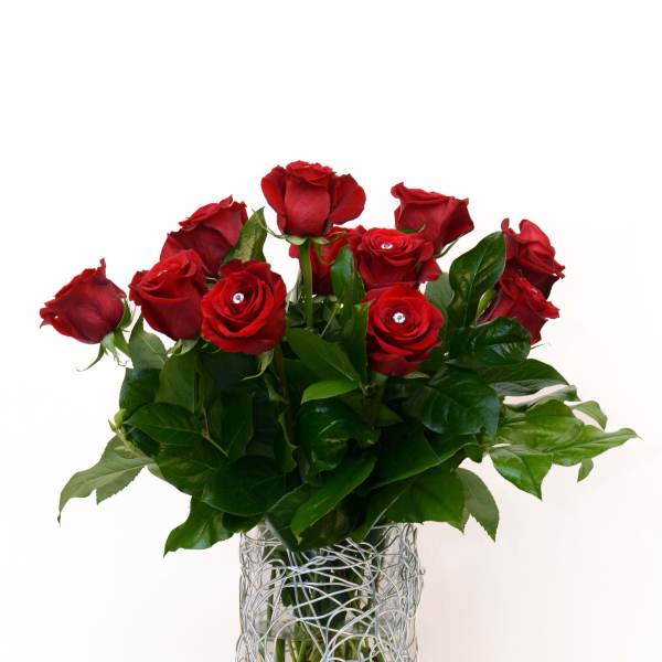 Red roses arranged in a clear glass vase with a silver wire wrap