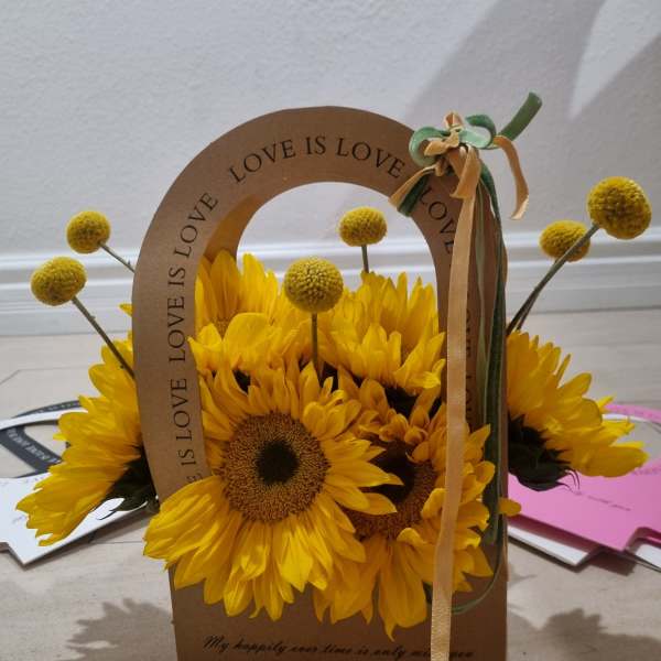 Yellow sunflowers arranged in a cardboard gift bag with a ribbon bow