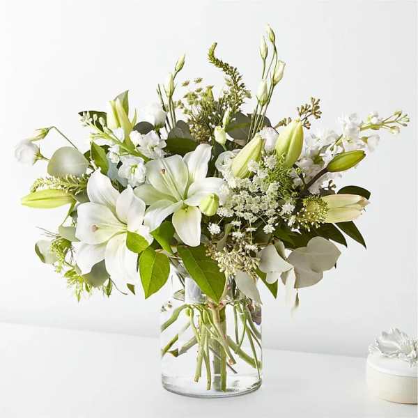 White lilies and mixed white flowers in a clear glass vase