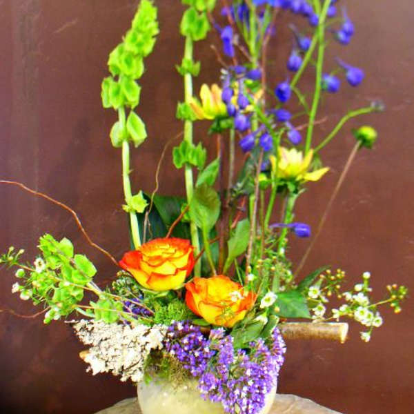 Tall mixed flower arrangement in a round vase with orange roses and blue blooms