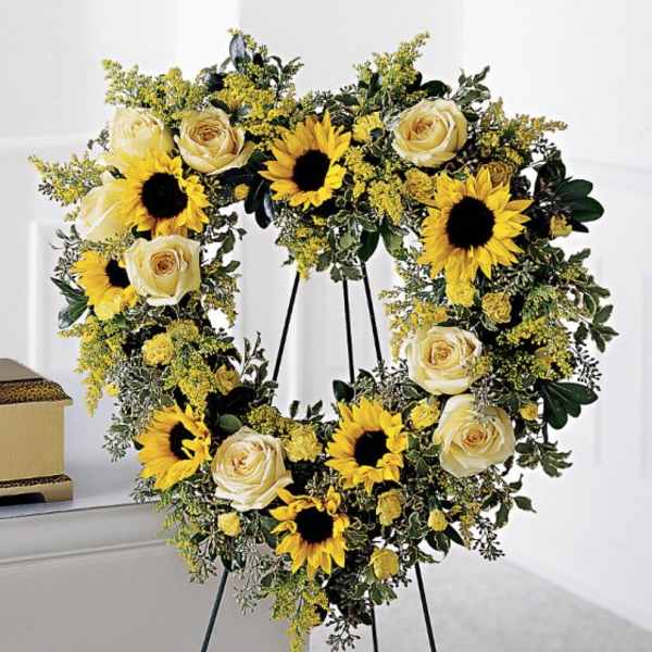 Heart-shaped floral wreath with sunflowers and cream roses on a stand