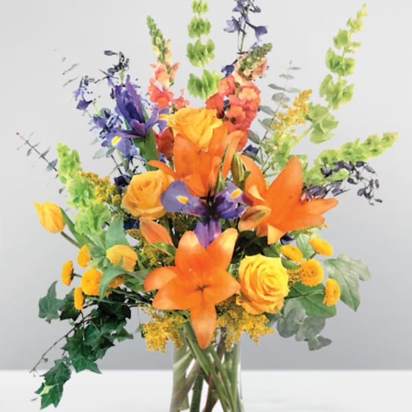 Mixed bouquet of orange, yellow, and purple flowers in a clear glass vase