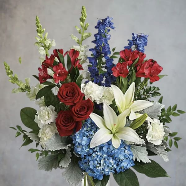 Bouquet of red roses, white lilies, blue hydrangeas, and red alstroemeria in a glass vase