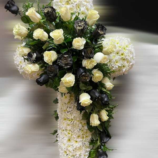 Standing cross of white chrysanthemums with cream and black roses clustered at the center.
