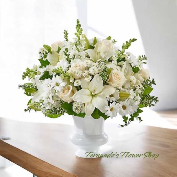White and cream lilies, roses, and daisies arranged in a white pedestal vase