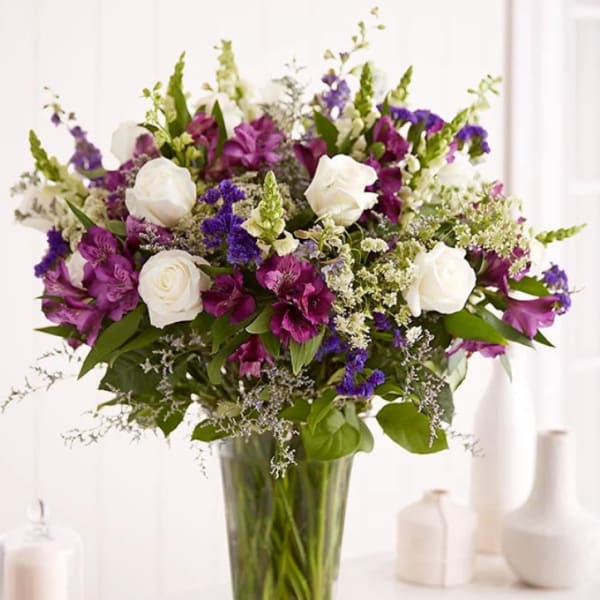 Tall arrangement of white roses and purple blooms in a clear glass vase