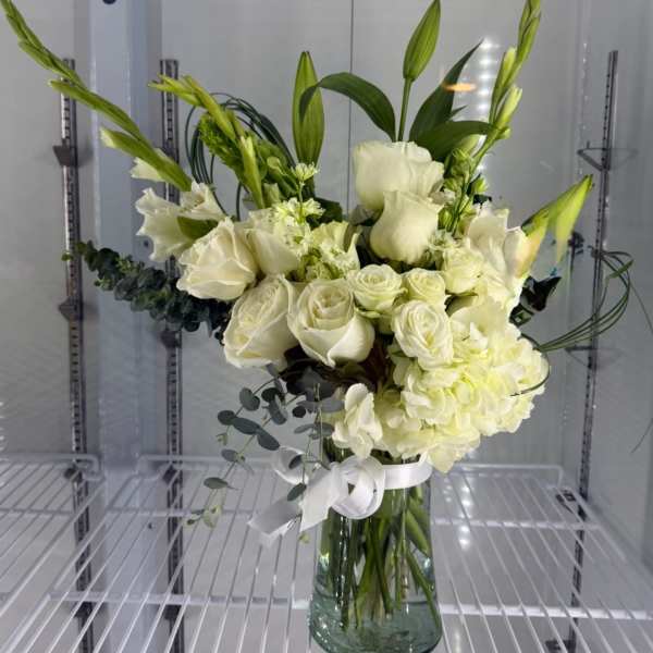 Tall arrangement of white roses, lilies, and hydrangea with green buds in a clear glass vase.